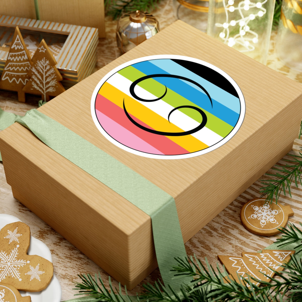 Gift box with a green ribbon on a festive background with cookies and Christmas decorations. Cancer Queer pride sticker centered on the box.