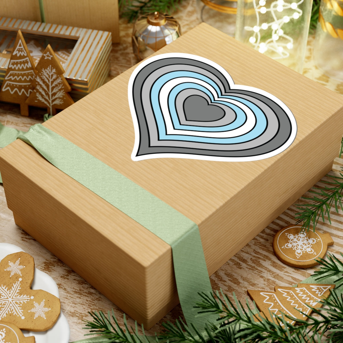 Gift box with a green ribbon on a festive background with cookies and Christmas decorations. Heart-shaped Demiboy pride sticker centered on the box.