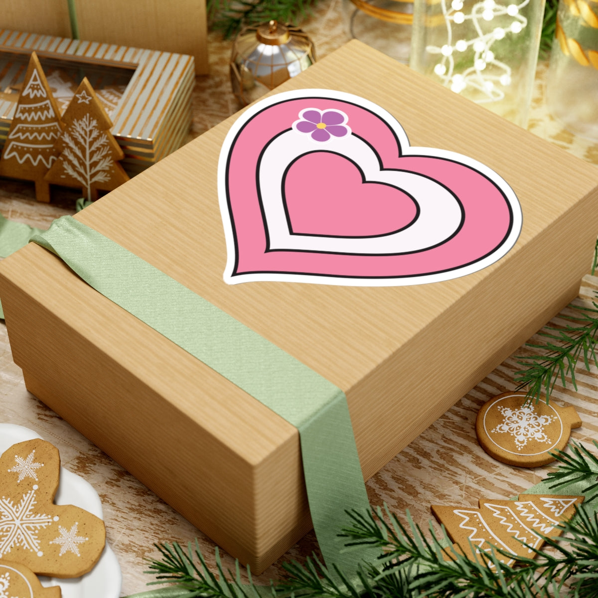 Gift box with a green ribbon on a festive background with cookies and Christmas decorations. Sapphic pride heart sticker centered on the box.