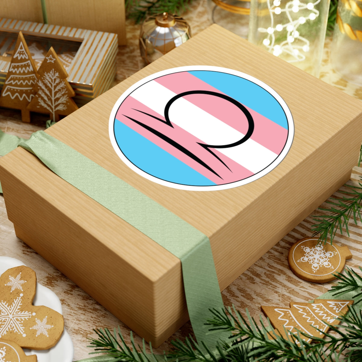 Gift box with a green ribbon on a festive background with cookies and Christmas decorations. Libra Transgender pride sticker centered on the box.
