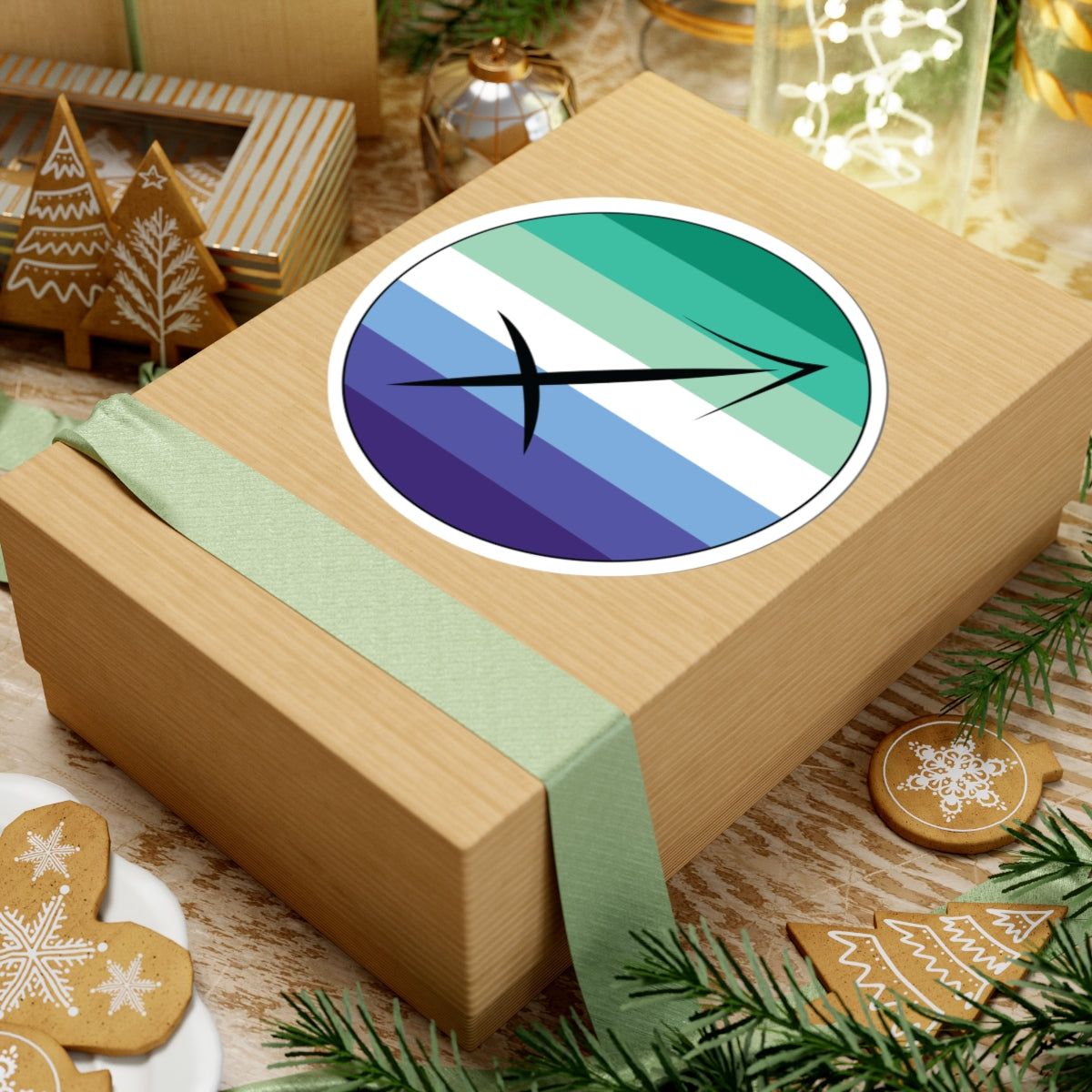 Gift box with a green ribbon on a festive background with cookies and Christmas decorations. Sagittarius Gay Men pride sticker centered on the box.