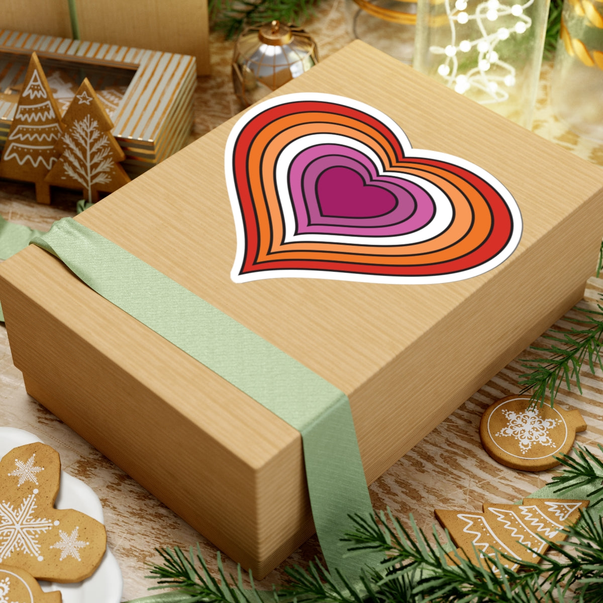 Gift box with a green ribbon on a festive table with cookies and decorations. Lesbian heart sticker centered on the box.
