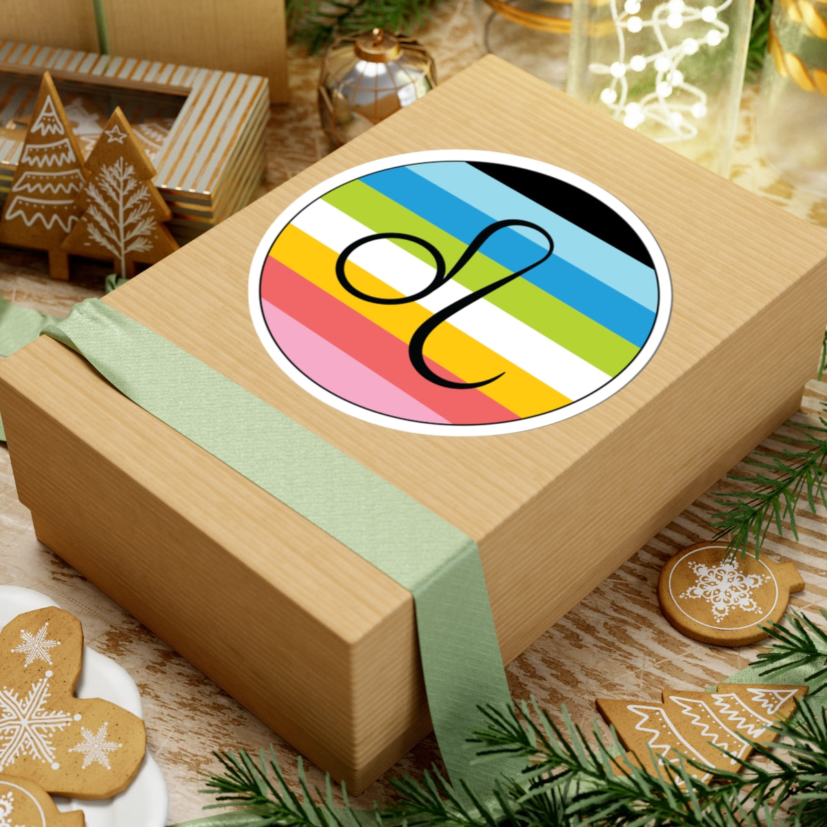 Gift box with a green ribbon on a festive background with cookies and Christmas decorations. Leo Queer pride sticker centered on the box.