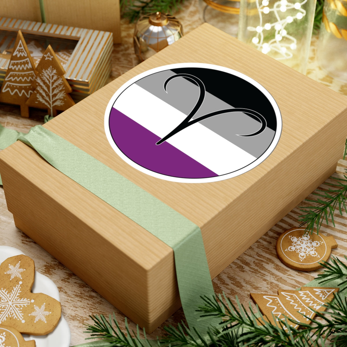 Gift box with a green ribbon on a festive background with cookies and Christmas decorations. Aires Asexual pride sticker centered on the box.