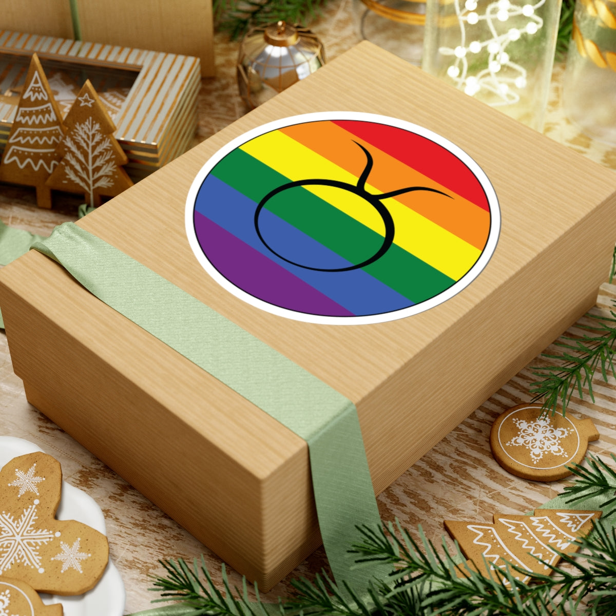 Gift box with a green ribbon on a festive background with cookies and Christmas decorations. Taurus Rainbow pride sticker centered on the box.