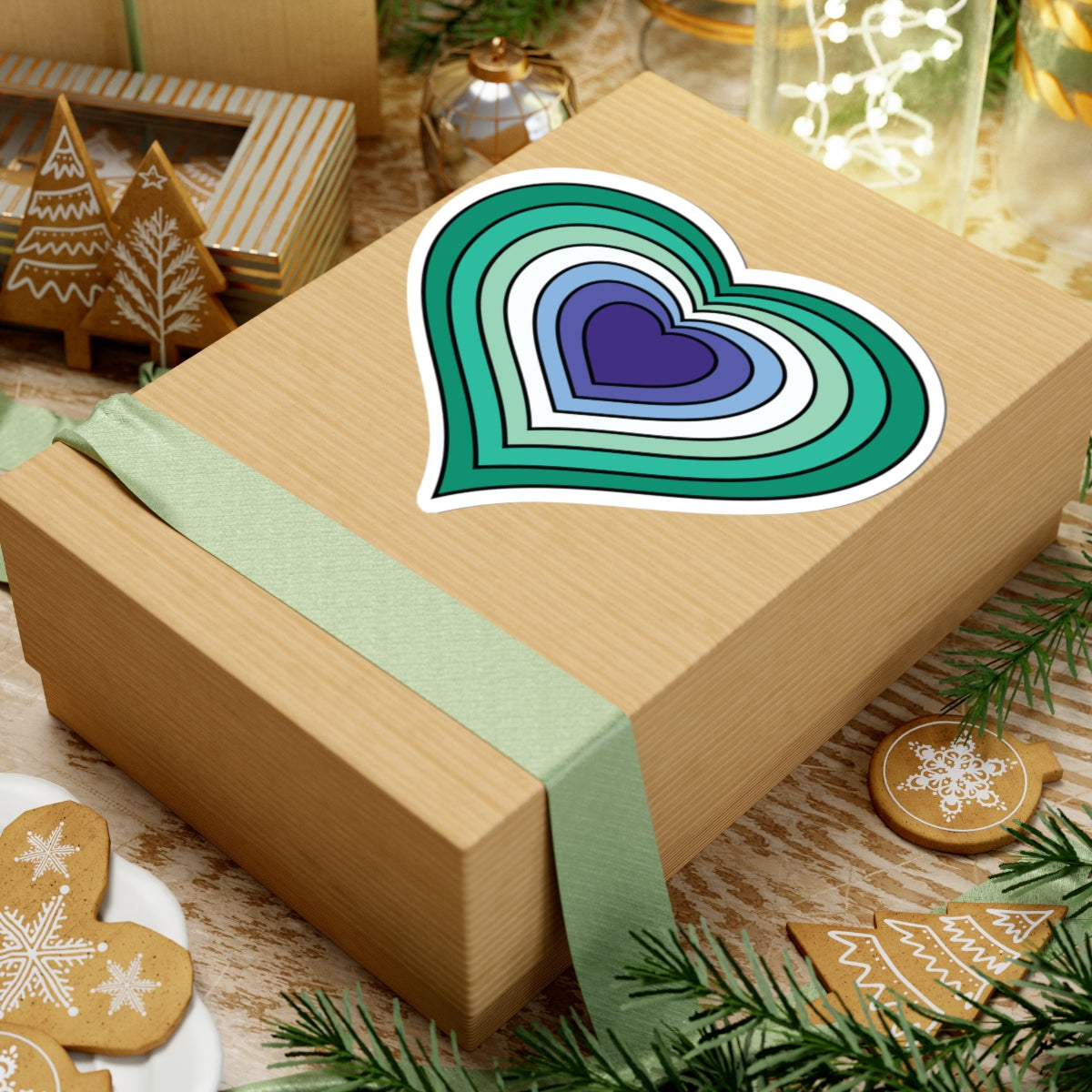 Gift box with a green ribbon on a festive background with cookies and Christmas decorations. Heart-shaped Gay Men pride sticker centered on the box.