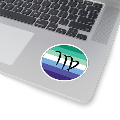 Close-up of the bottom right corner of a silver laptop featuring a 3 inch by 3 inch circular zodiac sticker with a centered Virgo glyph on a Gay Men pride flag style background applied to the surface.
