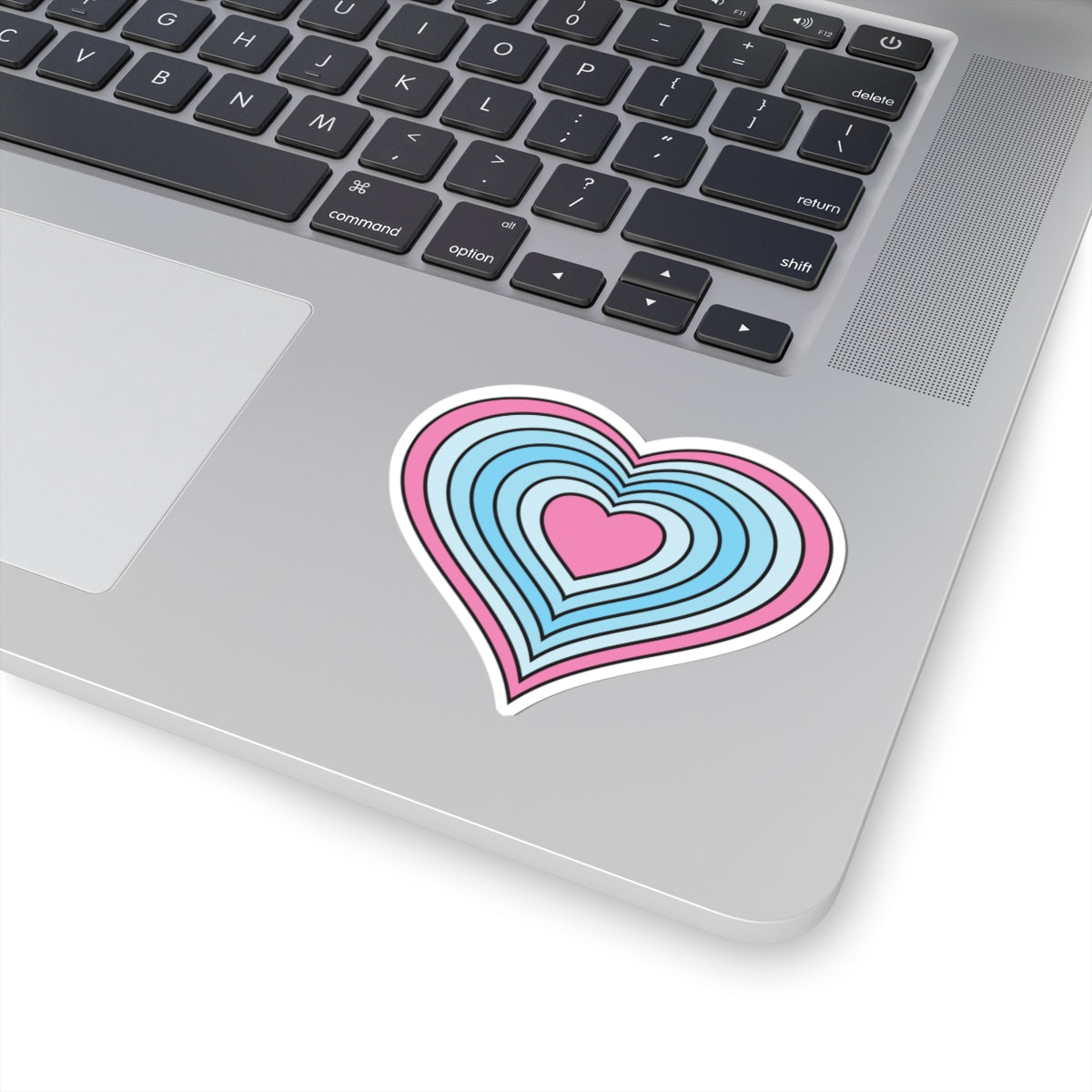 Close-up of the bottom right corner of a silver laptop featuring a 3 inch by 3 inch pride flag heart sticker in a Transmasc flag style applied to the surface.