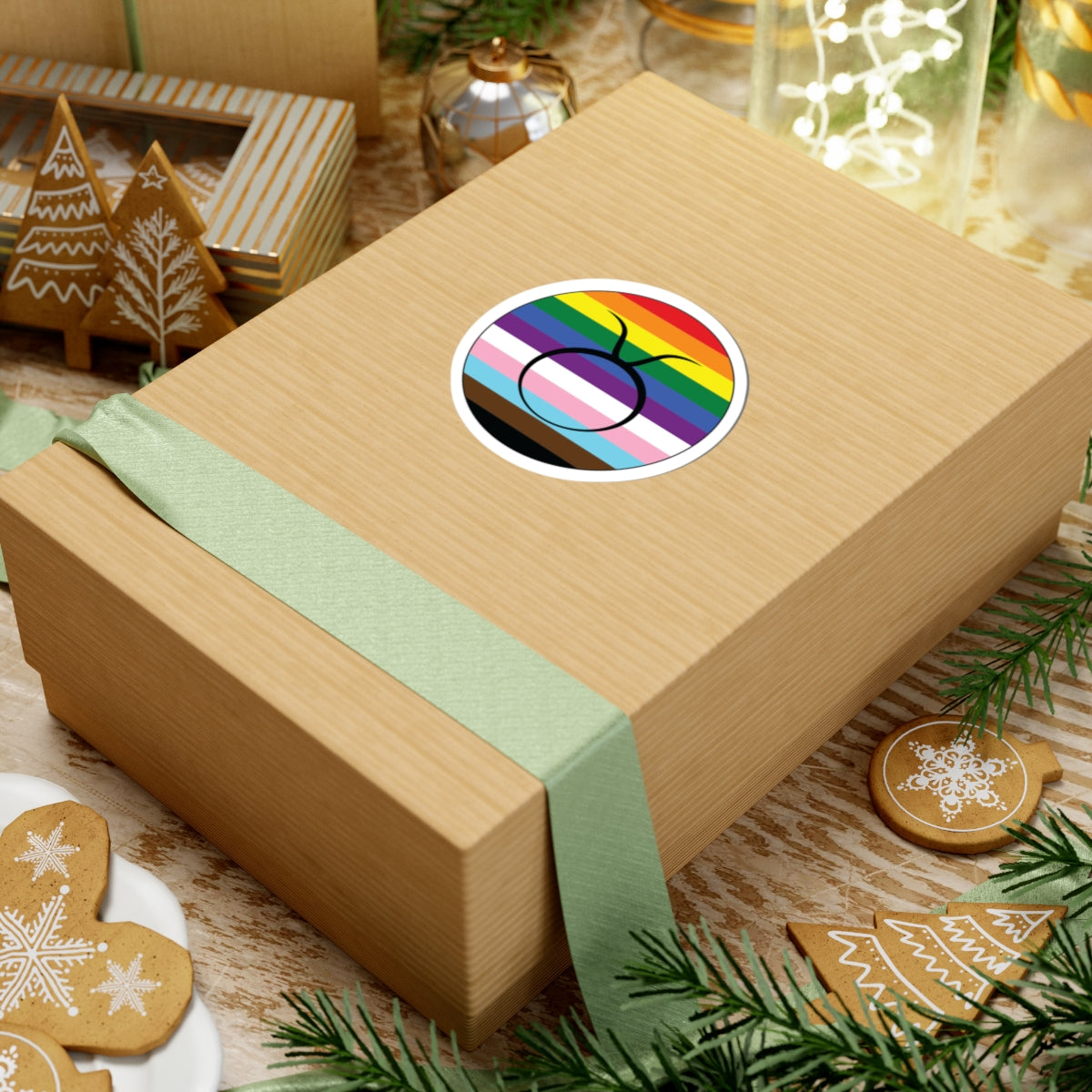 Gift box with a green ribbon on a festive background with cookies and Christmas decorations. Taurus Progress pride sticker centered on the box.