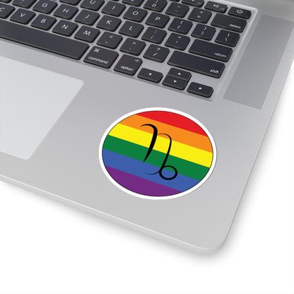 Close-up of the bottom right corner of a silver laptop featuring a 3 inch by 3 inch circular zodiac sticker with a centered Capricorn glyph on a Rainbow pride flag style background applied to the surface.