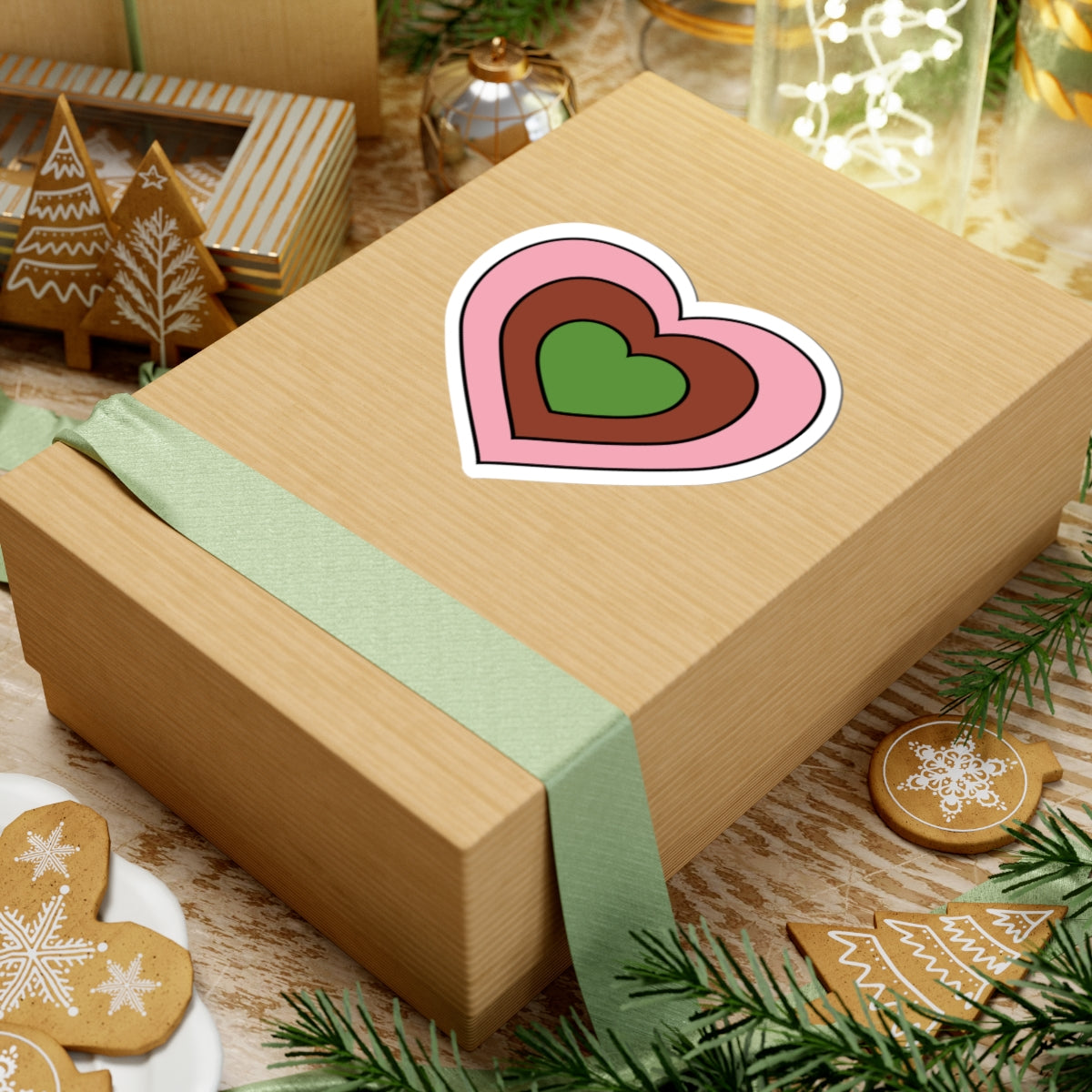 Gift box with a green ribbon on a festive background with cookies and Christmas decorations. Heart-shaped Gynesexual pride sticker centered on the box.