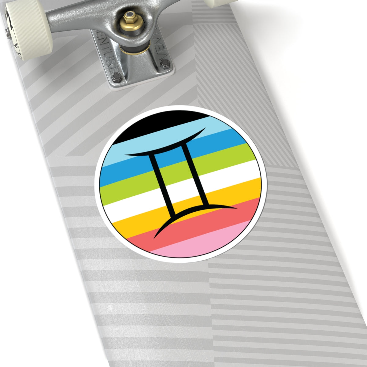 Close-up of the bottom of a silver skateboard featuring a 6 inch by 6 inch circular zodiac sticker with a centered Gemini glyph on a Queer pride flag style background applied to the surface.