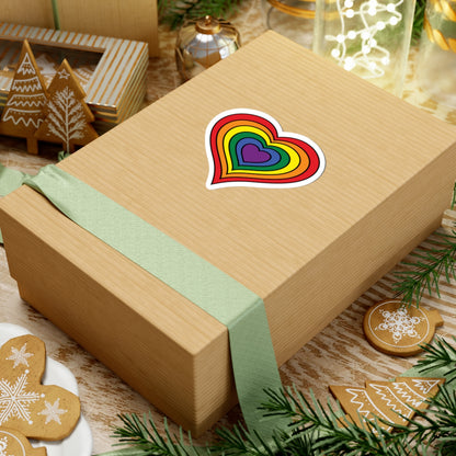 Gift box with a green ribbon on a festive background with cookies and Christmas decorations. Rainbow pride heart sticker centered on the box.