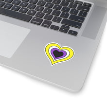Close-up of the bottom right corner of a silver laptop featuring a 2 inch by 2 inch pride flag heart sticker in a Nonbinary flag style applied to the surface.