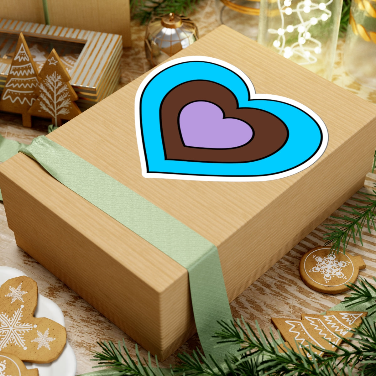 Gift box with a green ribbon on a festive background with cookies and Christmas decorations. Heart-shaped Androsexual pride sticker centered on the box.