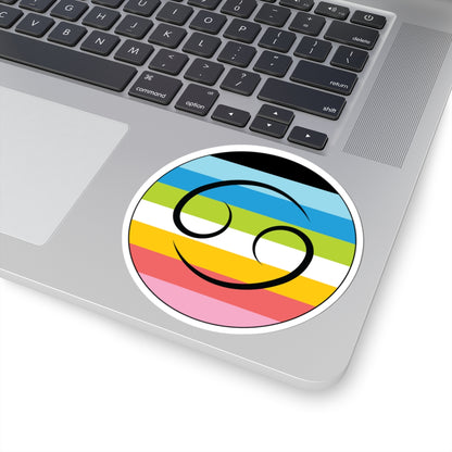 Close-up of the bottom right corner of a silver laptop featuring a 4 inch by 4 inch circular zodiac sticker with a centered Cancer glyph on a Queer pride flag style background applied to the surface.