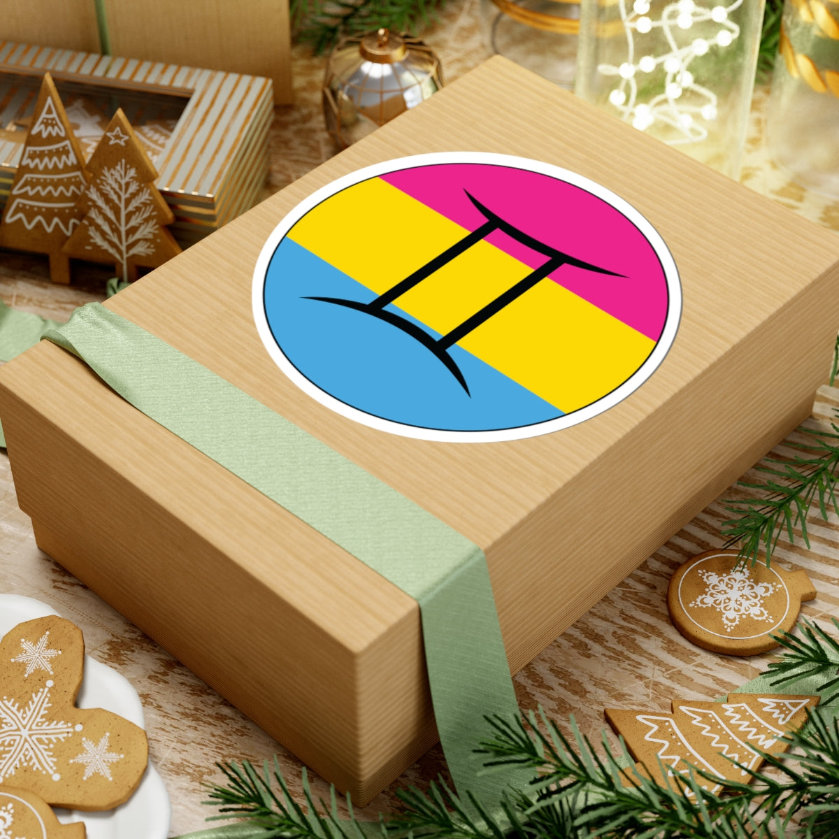 Gift box with a green ribbon on a festive background with cookies and Christmas decorations. Gemini Pansexual pride sticker centered on the box.