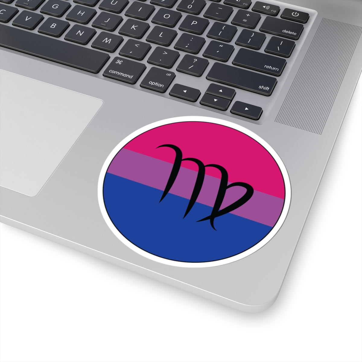 Close-up of the bottom right corner of a silver laptop featuring a 4 inch by 4 inch circular zodiac sticker with a centered Virgo glyph on a Bisexual pride flag style background applied to the surface.