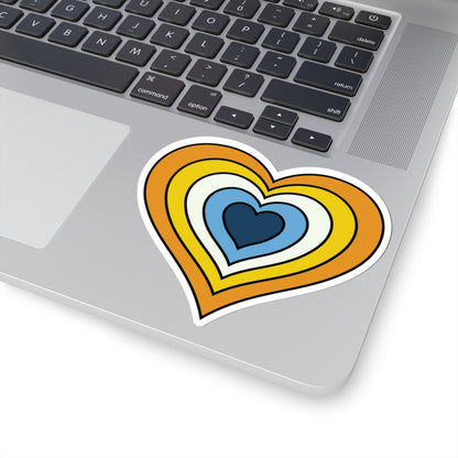 Close-up of the bottom right corner of a silver laptop featuring a 4 inch by 4 inch pride flag heart sticker in an Aroace flag style applied to the surface.
