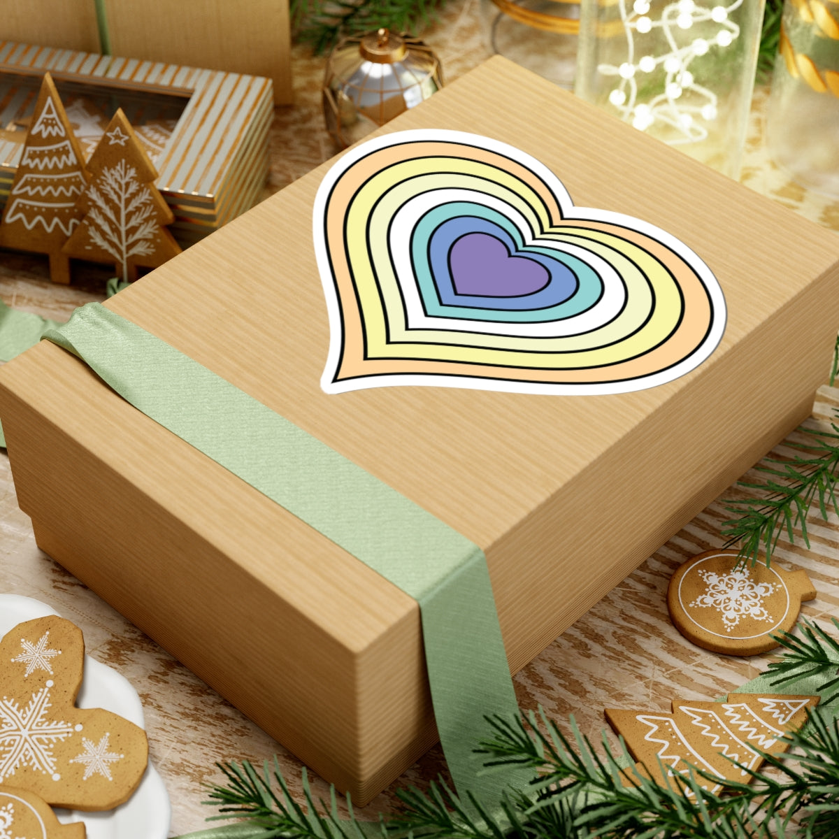 Gift box with a green ribbon on a festive background with cookies and Christmas decorations. Heart-shaped Genderfaun pride sticker centered on the box.