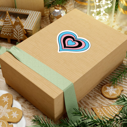 Gift box with a green ribbon on a festive background with cookies and Christmas decorations. Heart-shaped Transfeminine pride sticker centered on the box.