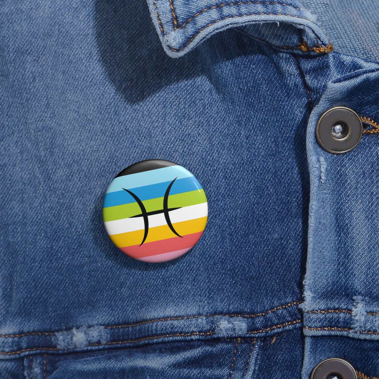 Close-up of a white circular pride button featuring the Pisces zodiac glyph centered over a queer pride flag background in pinks, yellow, white, green, blues, and black, attached to a blue denim jacket at the right chest with the button clearly visible.