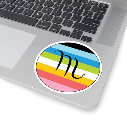 Close-up of the bottom right corner of a silver laptop featuring a 4 inch by 4 inch circular zodiac sticker with a centered Scorpio glyph on a Queer pride flag style background applied to the surface.