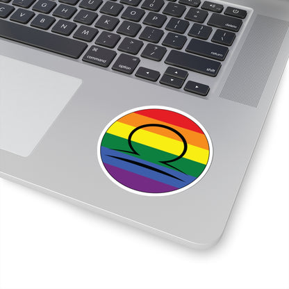 Close-up of the bottom right corner of a silver laptop featuring a 3 inch by 3 inch circular zodiac sticker with a centered Libra glyph on a Rainbow pride flag style background applied to the surface.