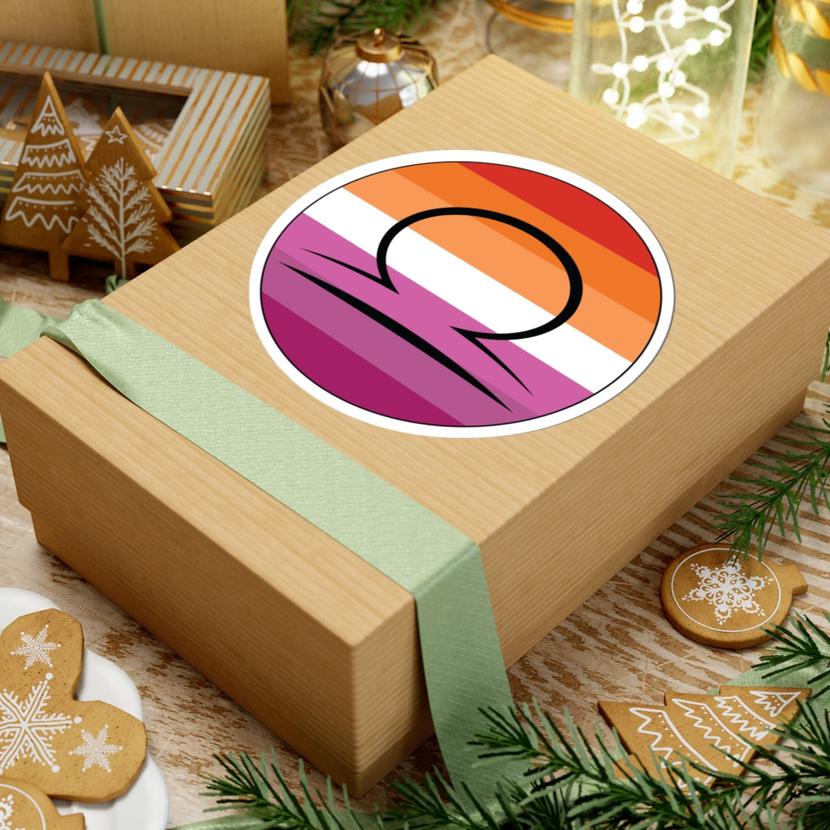 Gift box with a green ribbon on a festive background with cookies and Christmas decorations. Libra Lesbian pride sticker centered on the box.