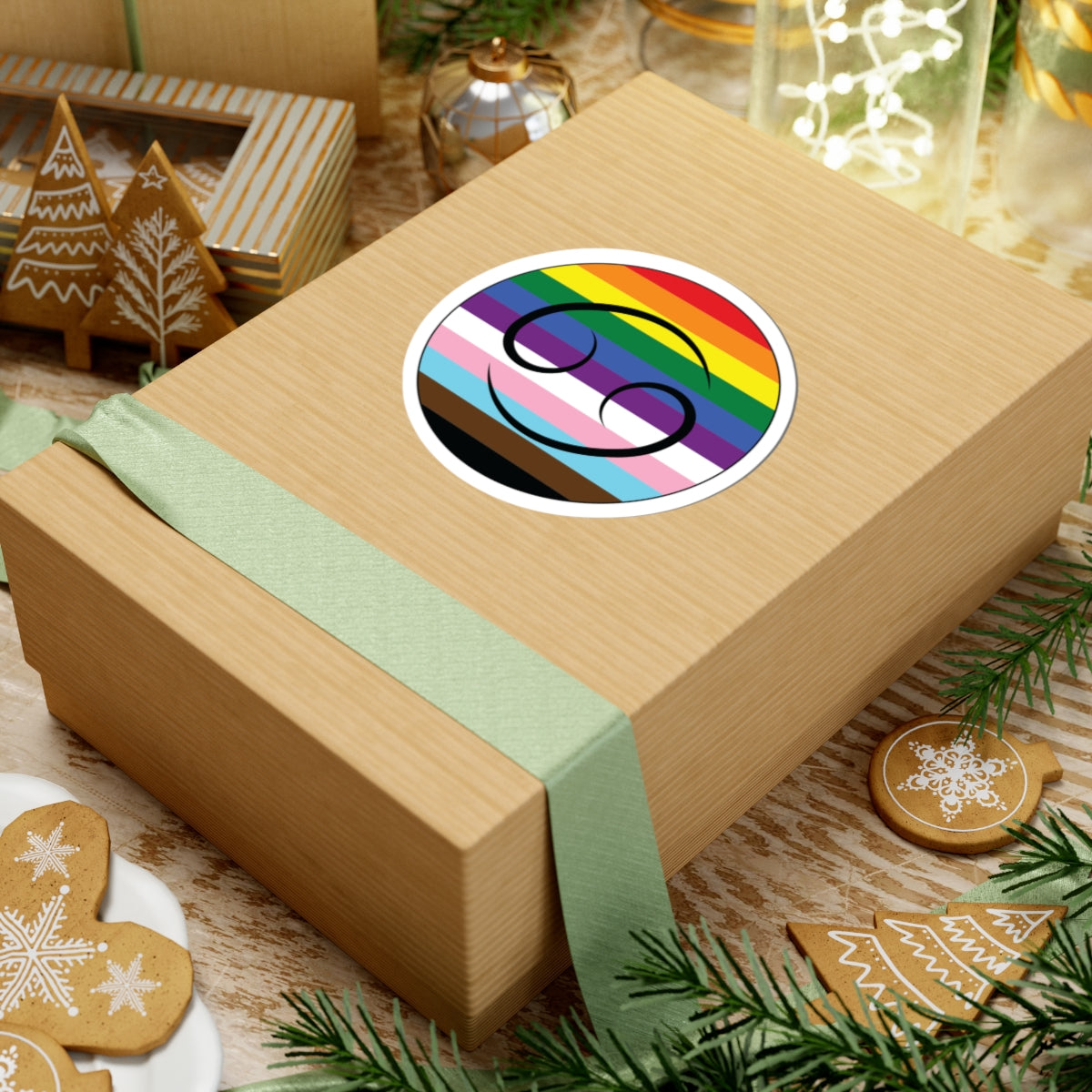 Gift box with a green ribbon on a festive background with cookies and Christmas decorations. Cancer Progress pride sticker centered on the box.