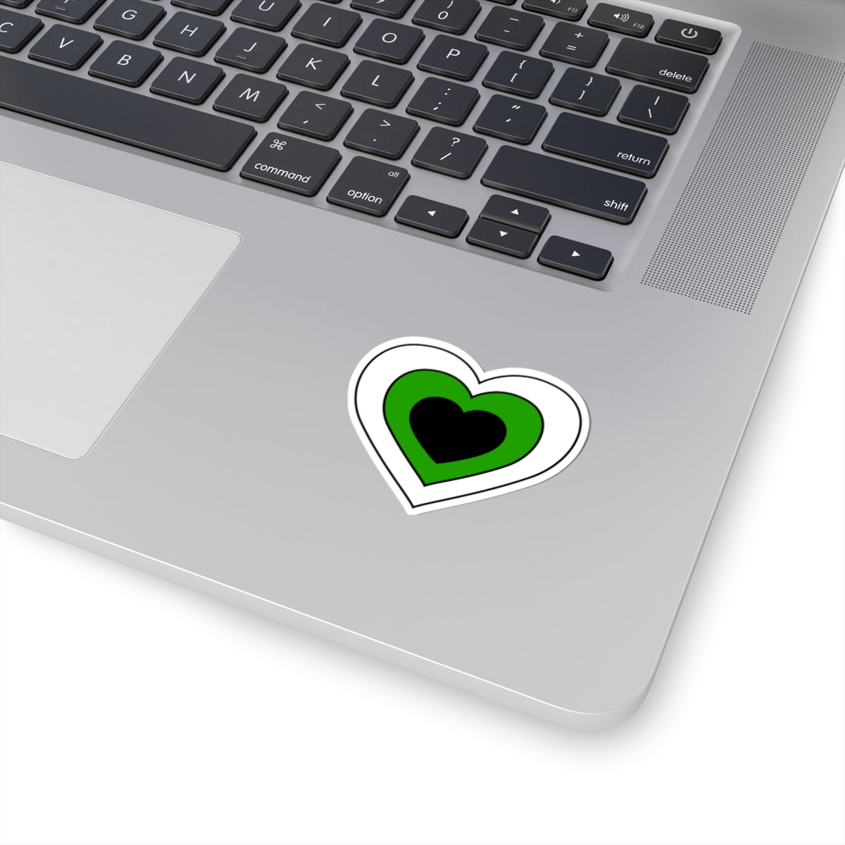 Close-up of the bottom right corner of a silver laptop featuring a 2 inch by 2 inch pride flag heart sticker in a Neutrois flag style applied to the surface.
