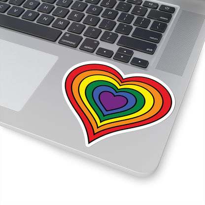 Close-up of the bottom right corner of a silver laptop featuring a 4 inch by 4 inch pride flag heart sticker in a rainbow pride flag style applied to the surface.