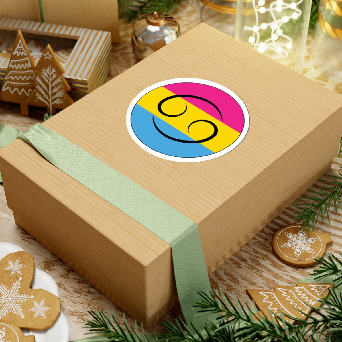 Gift box with a green ribbon on a festive background with cookies and Christmas decorations. Cancer Pansexual pride sticker centered on the box.