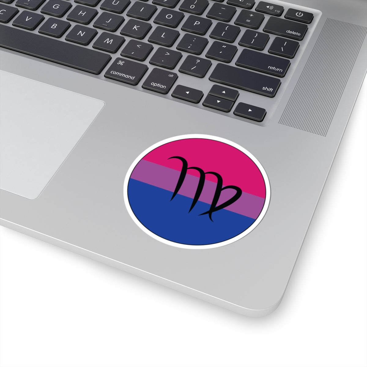 Close-up of the bottom right corner of a silver laptop featuring a 3 inch by 3 inch circular zodiac sticker with a centered Virgo glyph on a Bisexual pride flag style background applied to the surface.