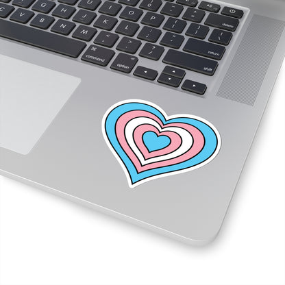 Close-up of the bottom right corner of a silver laptop featuring a 3 inch by 3 inch pride flag heart sticker in a Transgender flag style applied to the surface.