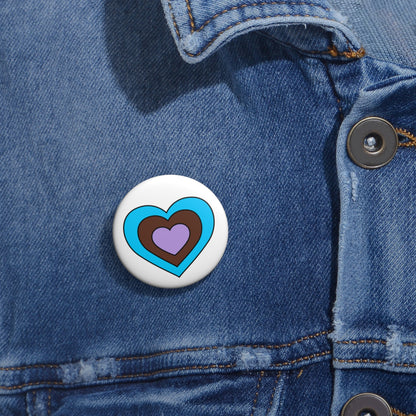Close-up of a white circular pride button featuring a nested heart design inspired by the Androsexual pride flag in blue, brown and lavender, attached to a blue denim jacket at the right chest with the button clearly visible.