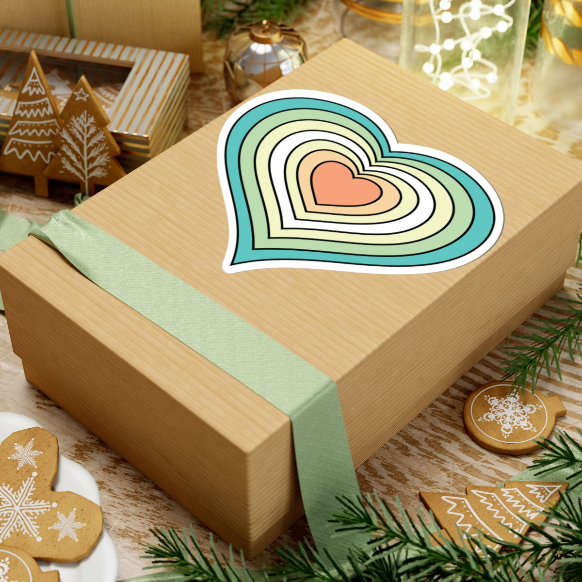 Gift box with a green ribbon on a festive background with cookies and Christmas decorations. Heart-shaped Genderfloren pride sticker centered on the box.
