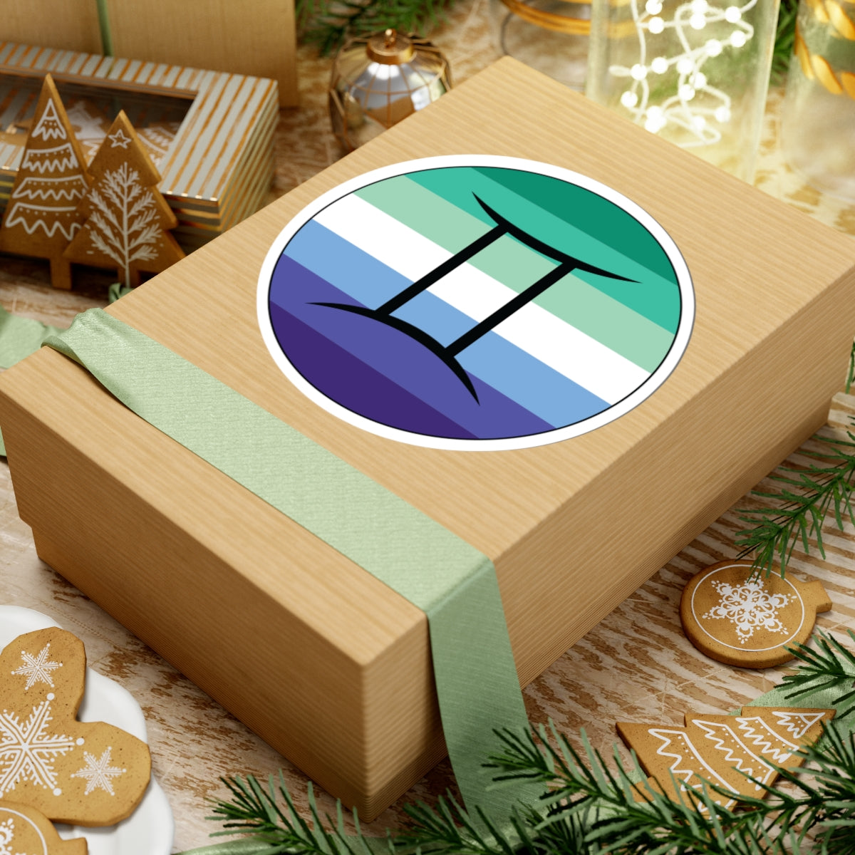 Gift box with a green ribbon on a festive background with cookies and Christmas decorations. Gemini Gay Men pride sticker centered on the box.
