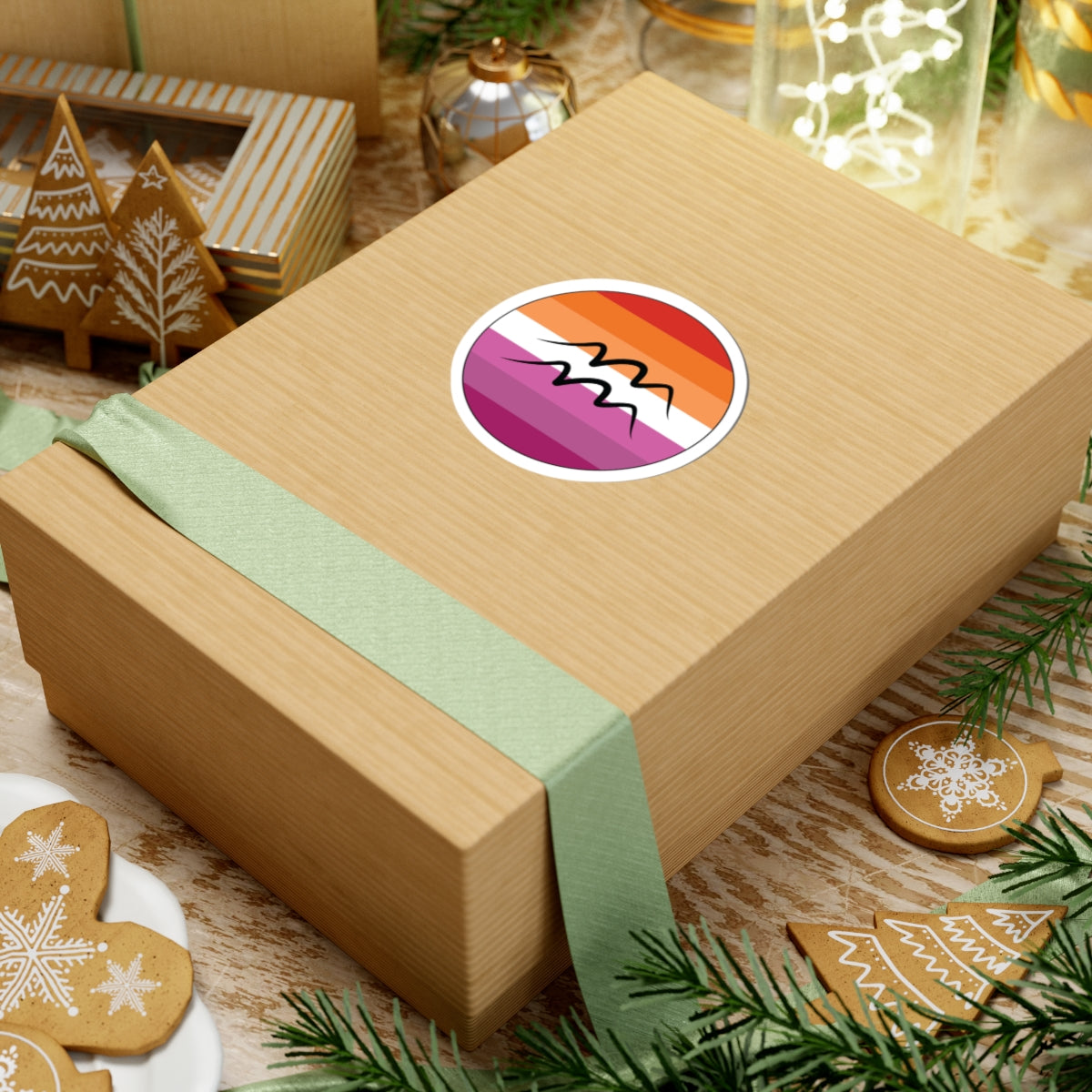Gift box with a green ribbon on a festive background with cookies and Christmas decorations. Aquarius Lesbian pride sticker centered on the box.