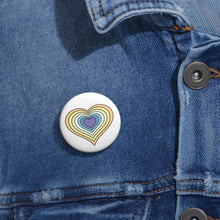 Close-up of a white circular pride button featuring a nested heart design inspired by the Genderfaun pride flag in yellows, white and blues, attached to a blue denim jacket at the right chest with the button clearly visible.