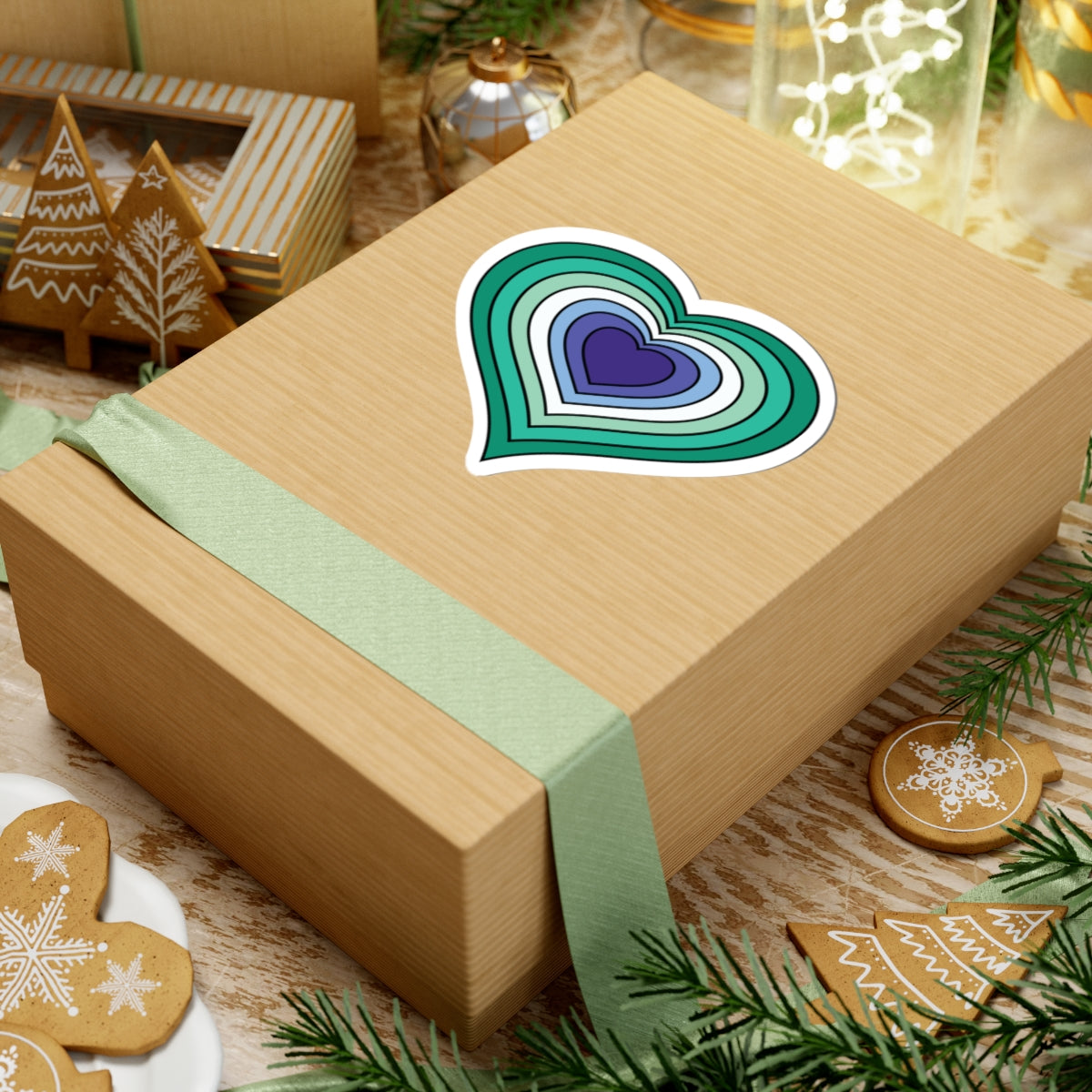 Gift box with a green ribbon on a festive background with cookies and Christmas decorations. Heart-shaped Gay Men pride sticker centered on the box.