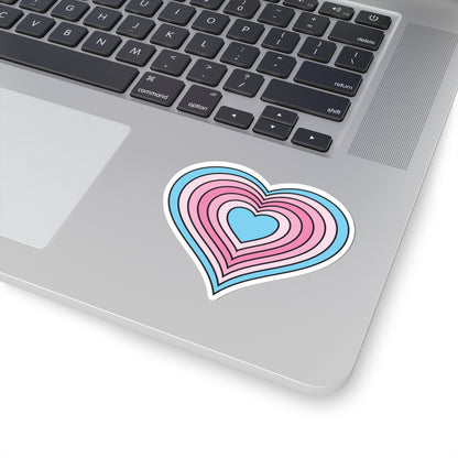 Close-up of the bottom right corner of a silver laptop featuring a 3 inch by 3 inch pride flag heart sticker in a Transfem flag style applied to the surface.