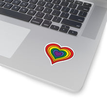 Close-up of the bottom right corner of a silver laptop featuring a 2 inch by 2 inch pride flag heart sticker in a rainbow pride flag style applied to the surface.