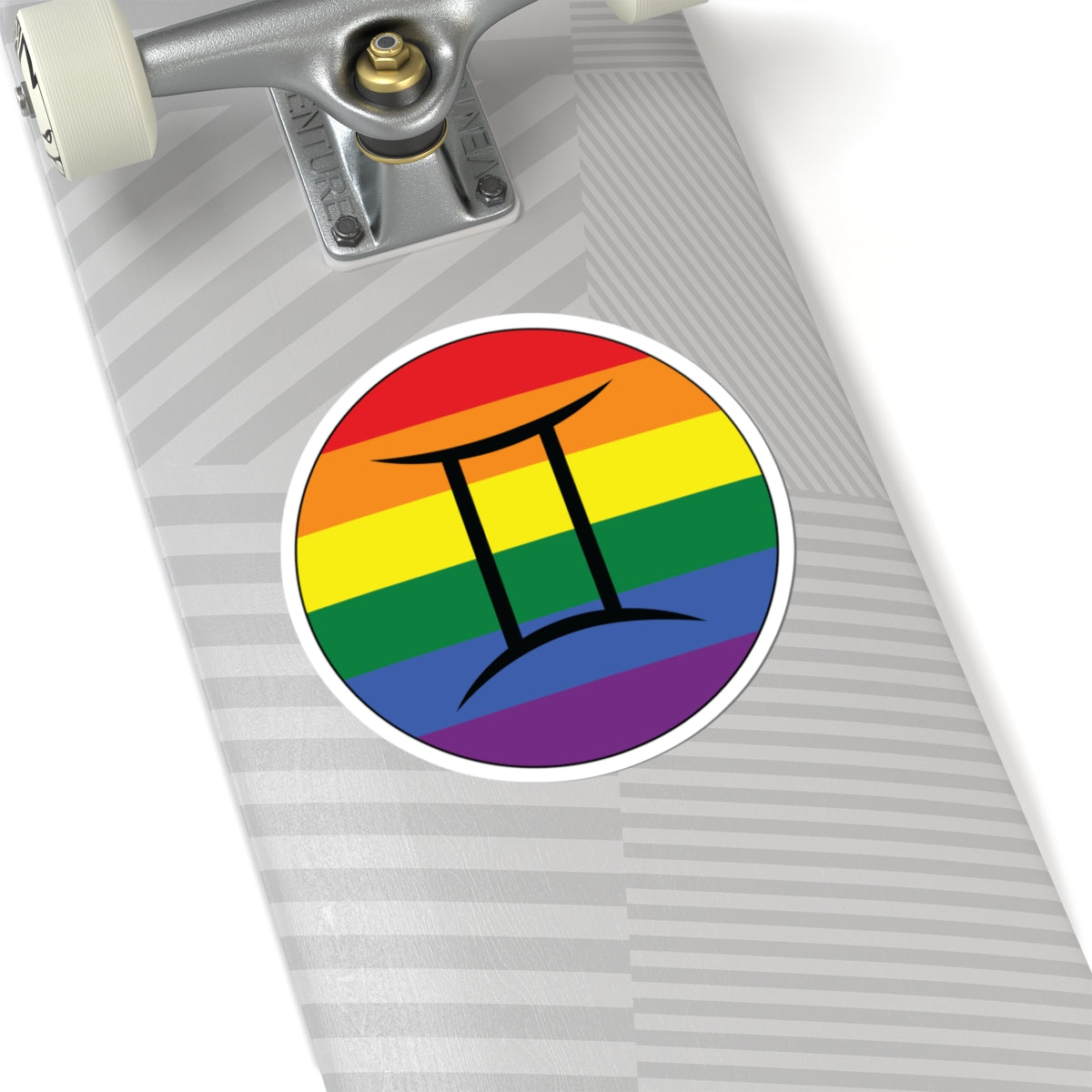 Close-up of the bottom of a silver skateboard featuring a 6 inch by 6 inch circular zodiac sticker with a centered Gemini glyph on a Rainbow pride flag style background applied to the surface.