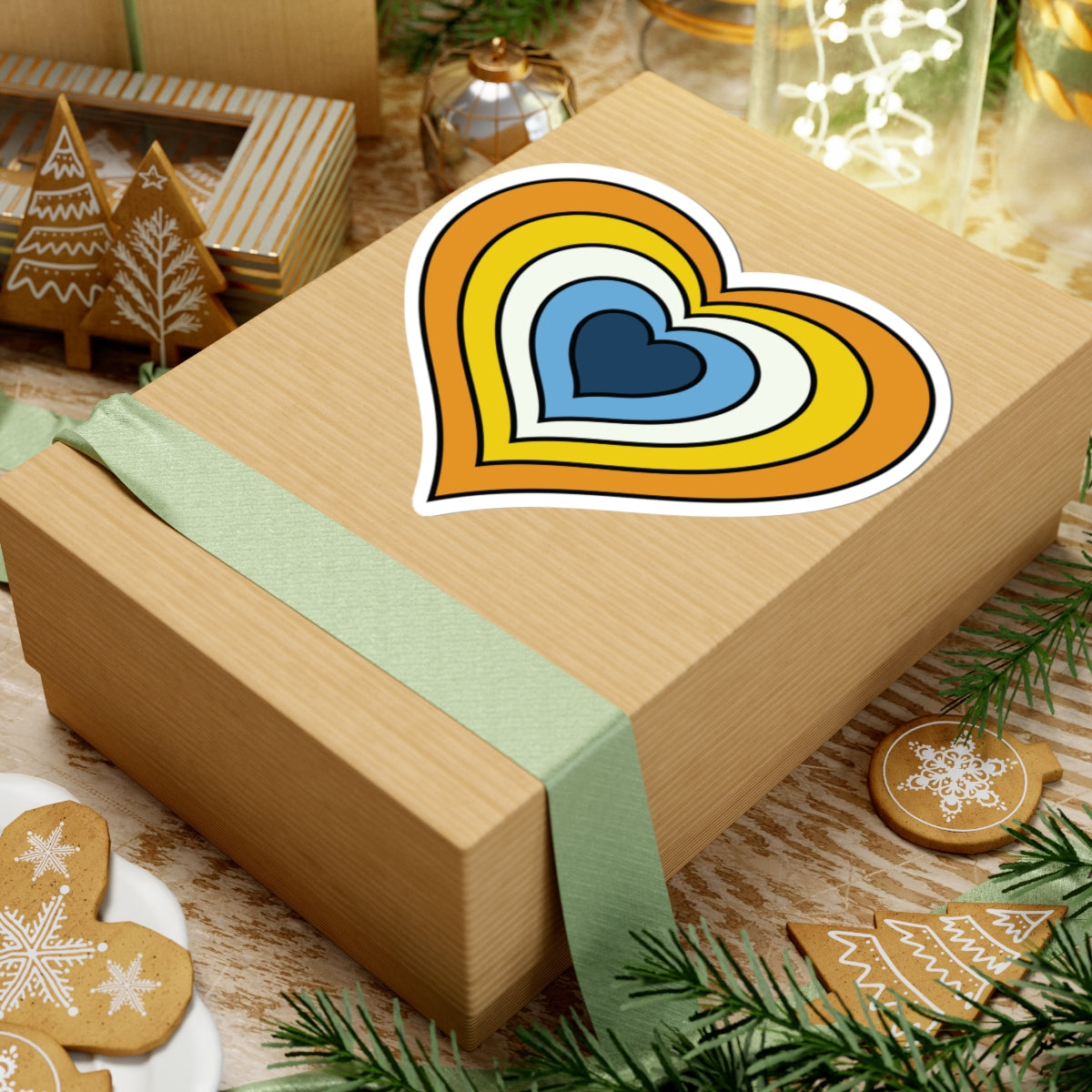 Gift box with a green ribbon on a festive background with cookies and Christmas decorations. Heart-shaped Aroace pride sticker centered on the box.