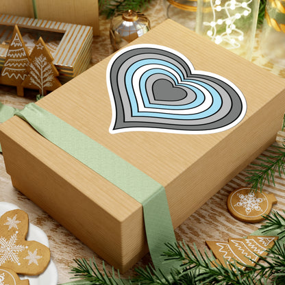 Gift box with a green ribbon on a festive background with cookies and Christmas decorations. Heart-shaped Demiboy pride sticker centered on the box.