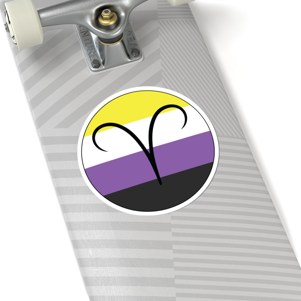 Close-up of the bottom of a silver skateboard featuring a 6 inch by 6 inch circular zodiac sticker with a centered Aires glyph on a Nonbinary pride flag style background applied to the surface.