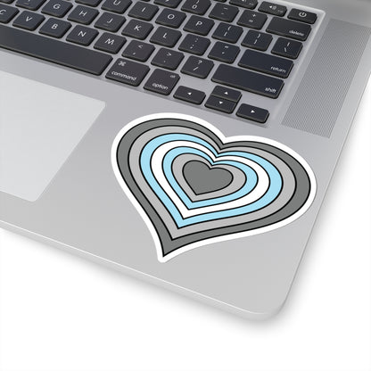 Close-up of the bottom right corner of a silver laptop featuring a 4 inch by 4 inch pride flag heart sticker in a Demiboy flag style applied to the surface.