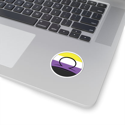 Close-up of the bottom right corner of a silver laptop featuring a 2 inch by 2 inch circular zodiac sticker with a centered Libra glyph on a Nonbinary pride flag style background applied to the surface.