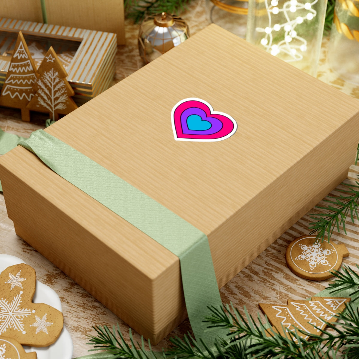 Gift box with a green ribbon on a festive background with cookies and Christmas decorations. Heart-shaped Androgyne pride sticker centered on the box.